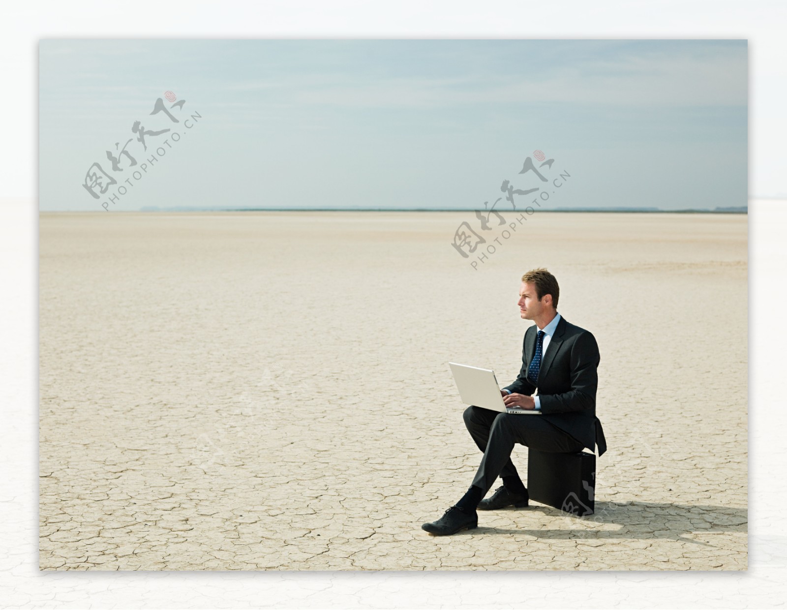 在沙漠中坐着皮箱玩电脑的外国商业男人图片